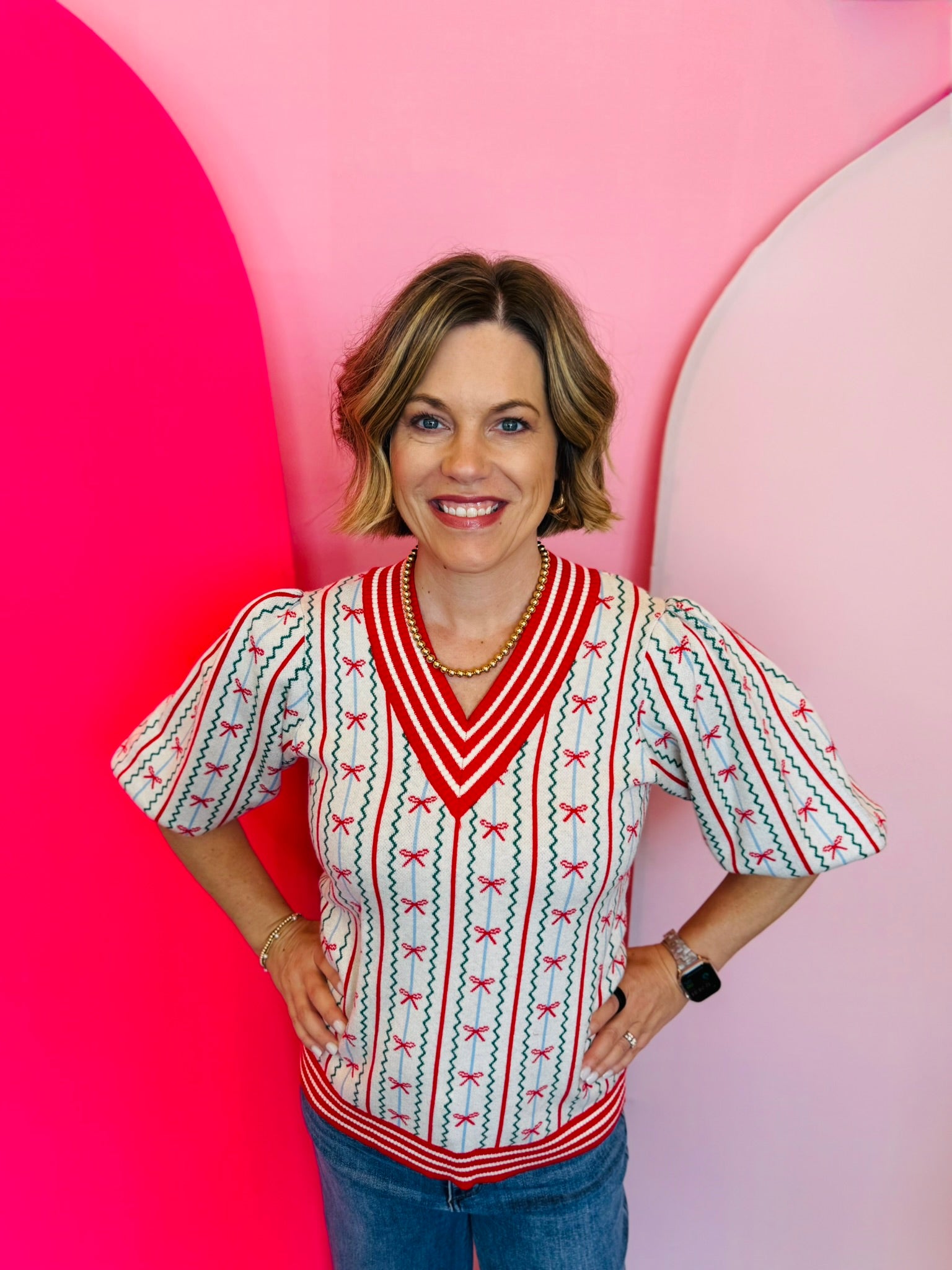 Cream colored sweater with red striped v-neck, sleeves, and hemline. Bow and zig zag pinstripe design.