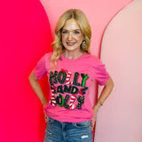 Bright pink holiday tee with glitter lettering, candy cane stripes, and holly accents.