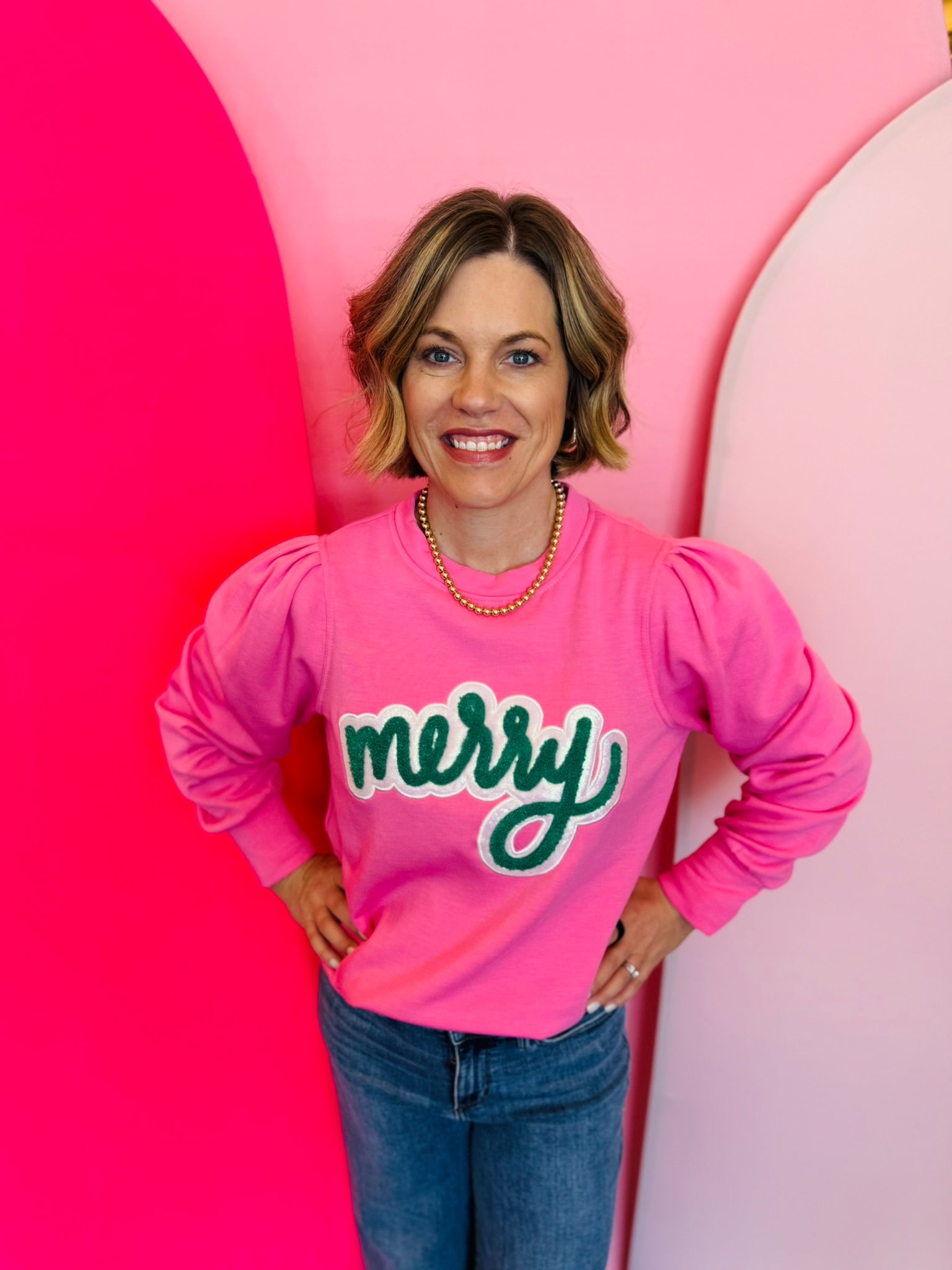 A pink sweatshirt with bold, textured green chenille lettering that spells "merry" across the chest.