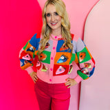 Rainbow colorblock sweater with sequin pie slices, pink buttons, and cropped relaxed fit.