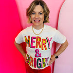 A vintage white t-shirt with "Merry & Bright Whimsy" in colorful, playful lettering.