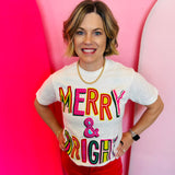 A vintage white t-shirt with "Merry & Bright Whimsy" in colorful, playful lettering.