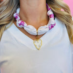 Close-up of the White & Fuchsia silky scarf necklace featuring a gold-trimmed, pearl-embellished heart charm, displayed to highlight color and detail.