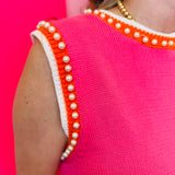 Zoomed-in image focusing on the pearl embellishments and orange/white striped neckline and sleeve hemline.