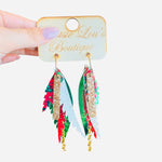 Green layered faux leather earrings with red glitter, poinsettia print, and gold chain accents.