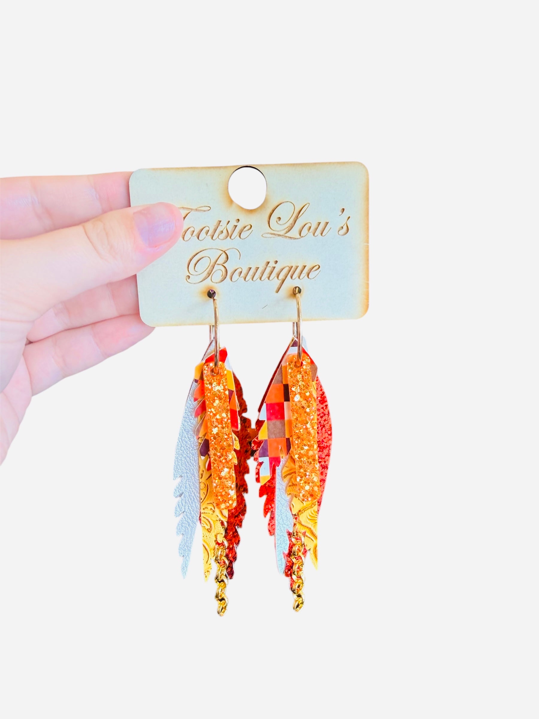Layered feather earrings in fall colors with plaid, glitter, textured leather, and gold chain accents.