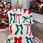 A cozy blanket featuring red and green bows on a festive background, adding holiday charm and warmth to any room.