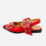 Red pointed-toe flats with bold silver double buckle straps and a slingback backstrap, combining vibrant color with edgy charm.