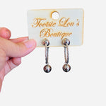 A pair of textured silver hoop earrings, each featuring a small, shiny silver sphere charm dangling from the bottom of the hoop.