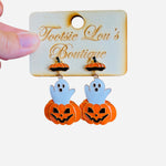 A pair of dangle earrings, each featuring a white cartoon ghost playfully popping out of the top of a carved orange jack-o'-lantern.