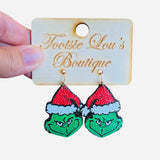 A pair of stud earrings, each featuring the Grinch's green face wearing a red and white Santa hat.
