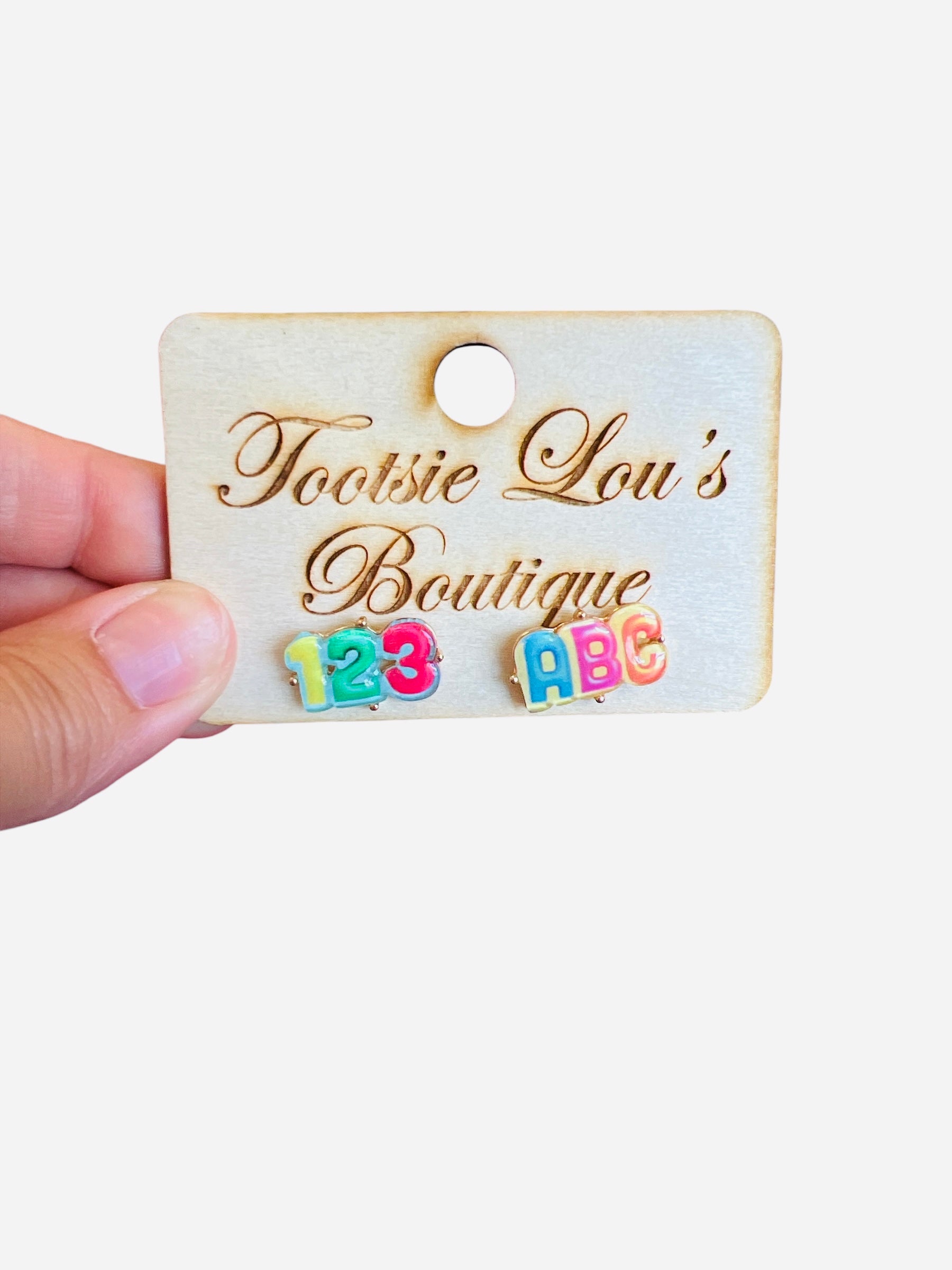 A pair of stud earrings with a white base. One earring features the letters "ABC" in colorful enamel, and the other features the numbers "123" in colorful enamel.