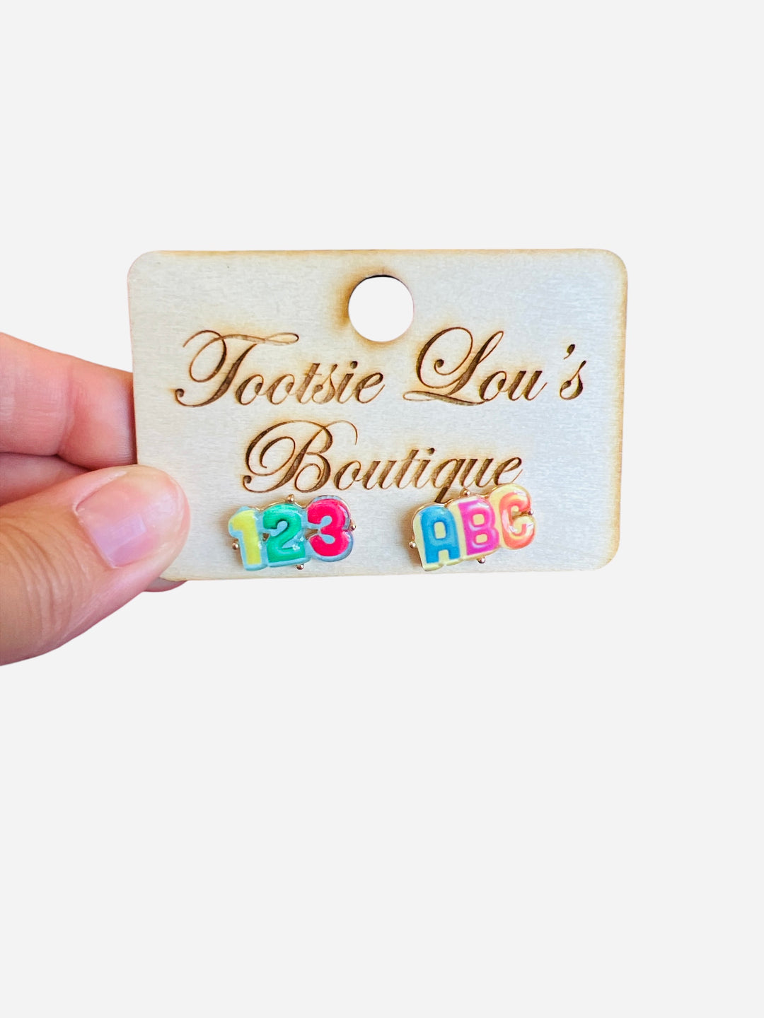 A pair of stud earrings with a white base. One earring features the letters "ABC" in colorful enamel, and the other features the numbers "123" in colorful enamel.