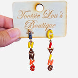A pair of dangle earrings with letter charms. One earring's charms spell out "THANKS" and the other spells out "GIVING" in fall colors, with a small scarecrow charm at the bottom of each.