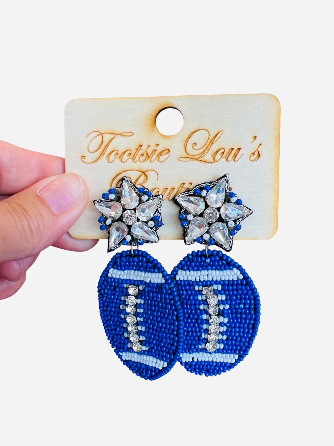 A pair of dangle earrings, each with a sparkling crystal star stud at the top. Dangling below is a football-shaped charm made from vibrant blue beads.