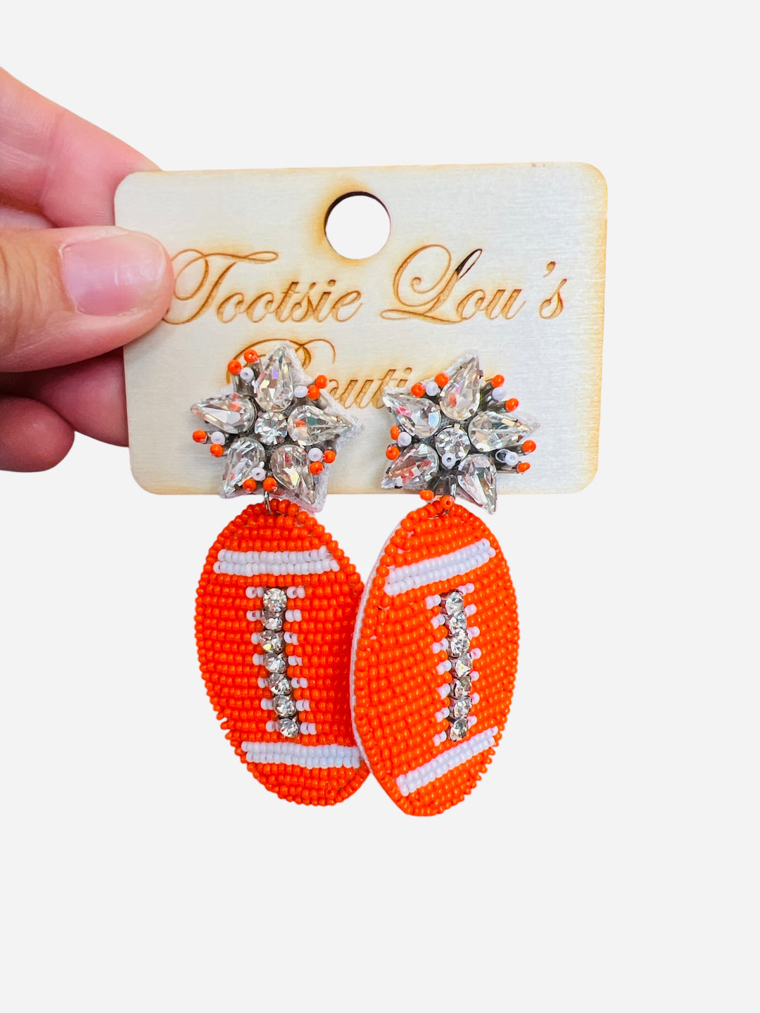 A pair of dangle earrings, each with a sparkling crystal star stud at the top. Dangling below is a football-shaped charm made from vibrant orange beads.