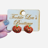 A pair of stud earrings shaped like small pumpkins. The pumpkins are covered in a pavé of small, sparkling red crystals and have a single green crystal at the top for the stem.
