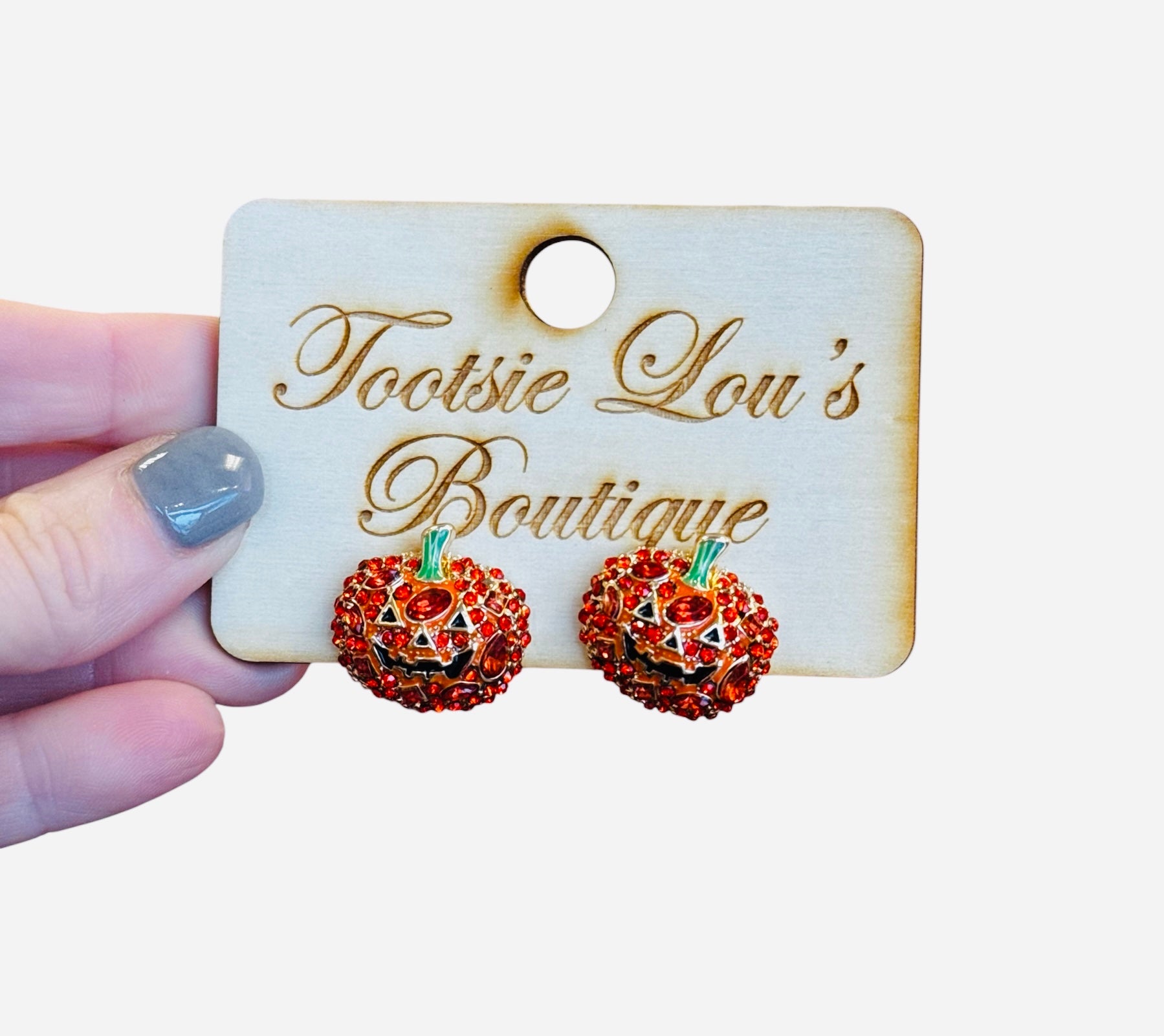 A pair of stud earrings shaped like small pumpkins. The pumpkins are covered in a pavé of small, sparkling red crystals and have a single green crystal at the top for the stem.