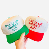 Red and green baseball hats with “Put It On Santa’s Tab” embroidery, festive Christmas accessory.