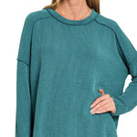 Plus-size teal ribbed boat neck long sleeve top with raw edge detailing.