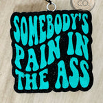 Black car freshie with teal text reading “Somebody’s Pain In The Ass.”