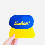 Blue hat with yellow bill and “Sunkissed” embroidered on front, adjustable strap in back