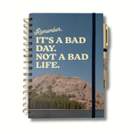 Blue hardcover journal with cream lettering that says “It’s A Bad Day. Not a Bad Life.” and features mountains with a lake, matching pen reading “I’ll Try Again Tomorrow,” A5 size, 140 pages.