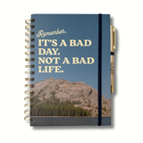 Blue hardcover journal with cream lettering that says “It’s A Bad Day. Not a Bad Life.” and features mountains with a lake, matching pen reading “I’ll Try Again Tomorrow,” A5 size, 140 pages.
