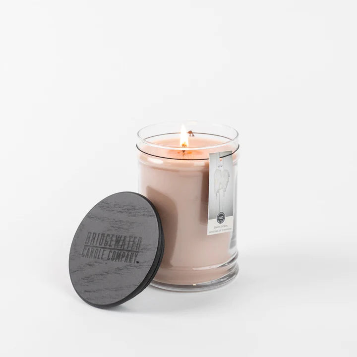 An 18oz large jar candle with a pink hue, burning with a visible wick, alongside a dark wooden lid