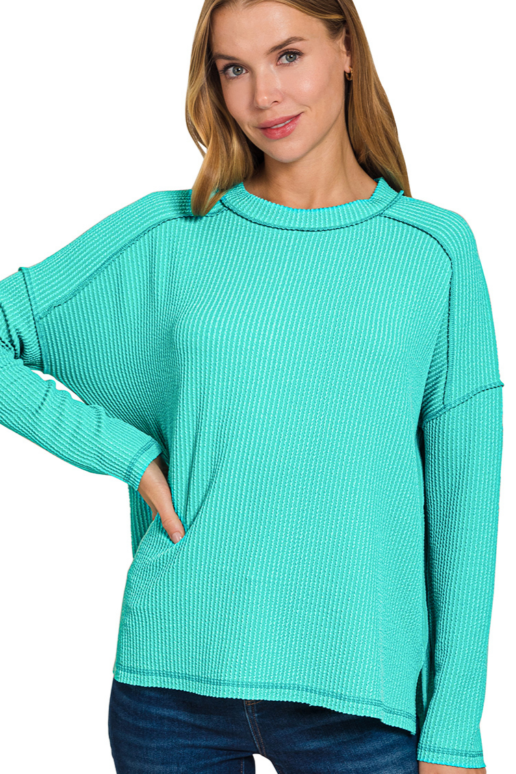 A turquoise ribbed boat neck top. The top has long sleeves, a relaxed fit, and raw edge details on the seams.