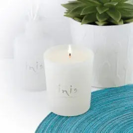 The 6.7 oz Inis Scented Candle in its frosted glass vessel, shown with a soft, glowing flame.