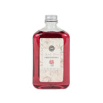 A bottle of Sweet Grace Flower Diffuser Oil Refill with a pinkish liquid visible through the clear glass and a label at the front.