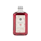 A bottle of Sweet Grace Flower Diffuser Oil Refill with a pinkish liquid visible through the clear glass and a label at the front.