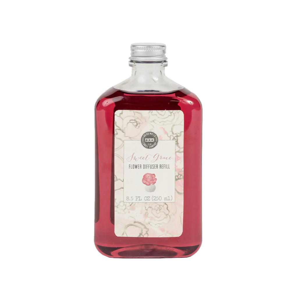 A bottle of Sweet Grace Flower Diffuser Oil Refill with a pinkish liquid visible through the clear glass and a label at the front.