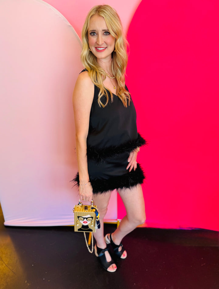 Side profile of the black feather cami paired with a purse, highlighting the feather trim, sleeveless fit, and flattering silhouette