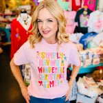 Light pink Christmas tee with colorful lettering, candy cane stripes, stars, and Christmas tree graphics.