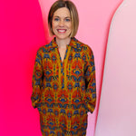 Toffee Boho Print Dress with orange, gold, and navy pattern, collared neckline, cotton braided trim, and pockets.