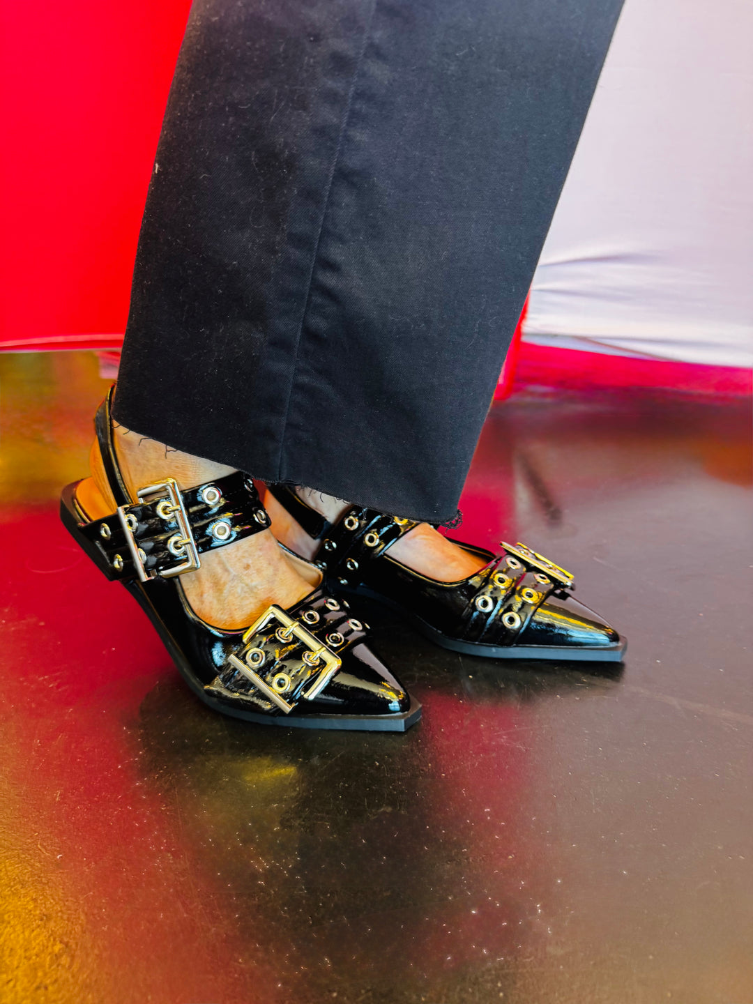 Black pointed-toe flats with bold silver double buckle straps and a slingback backstrap, combining vibrant color with edgy charm.