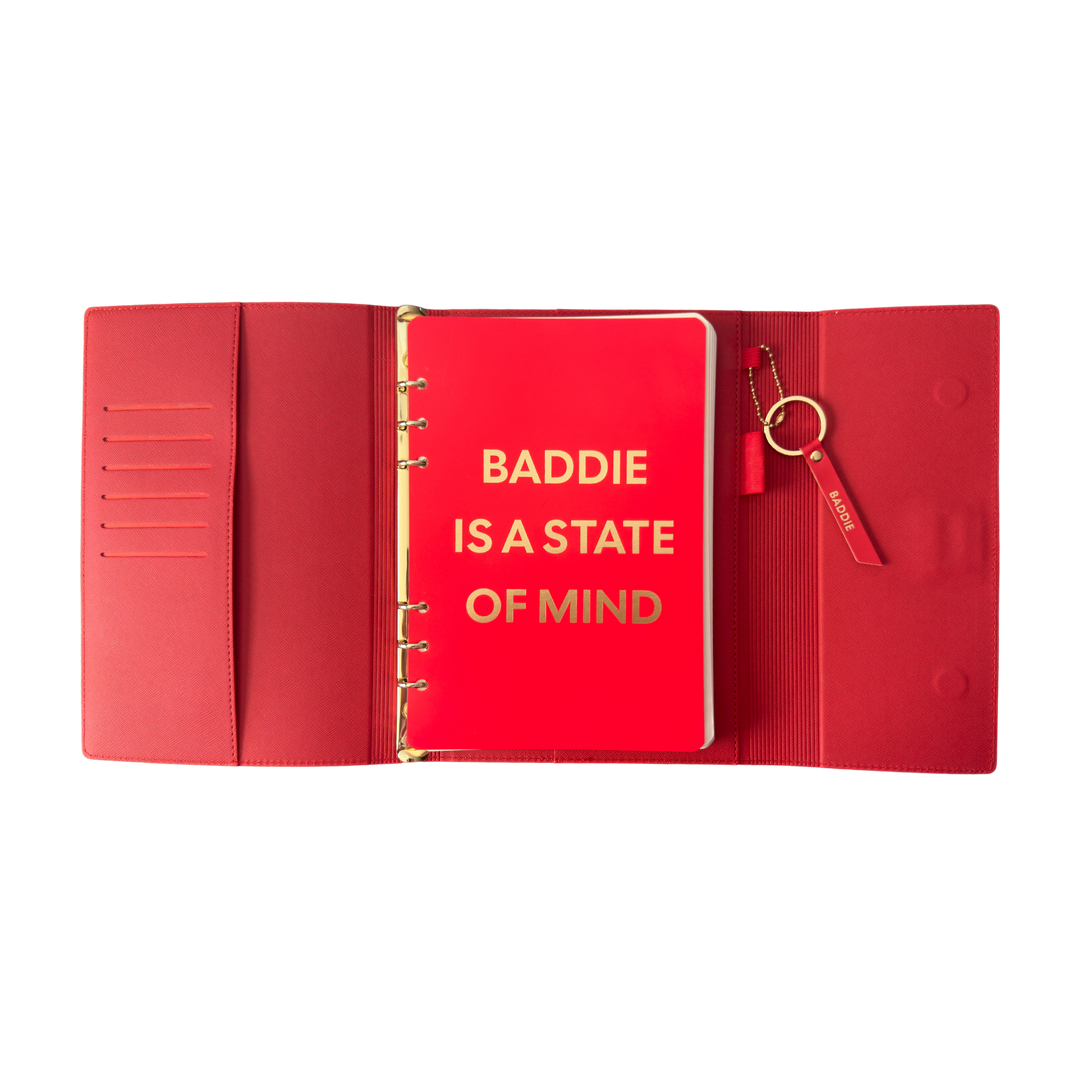 Red notebook with gold text 'BADDIE IS A STATE OF MIND' 
