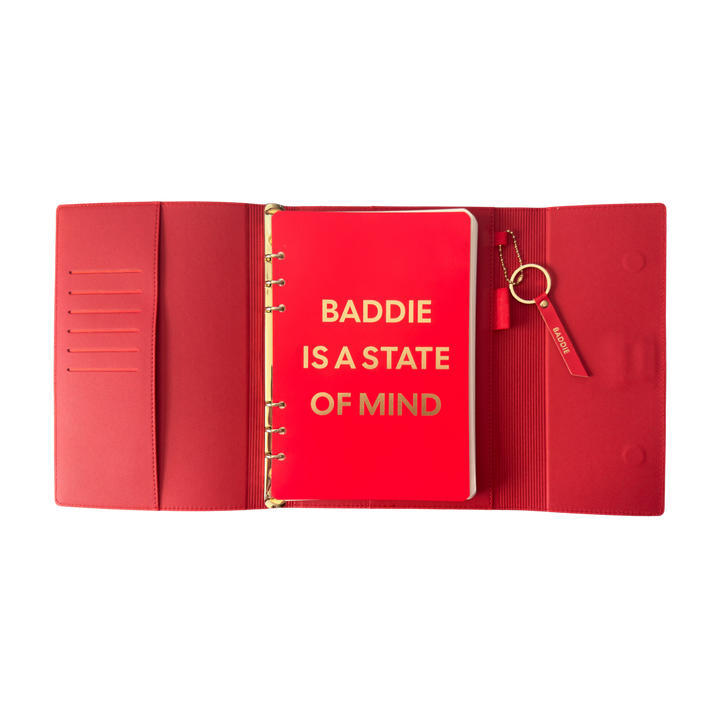 Red notebook with gold text 'BADDIE IS A STATE OF MIND' 