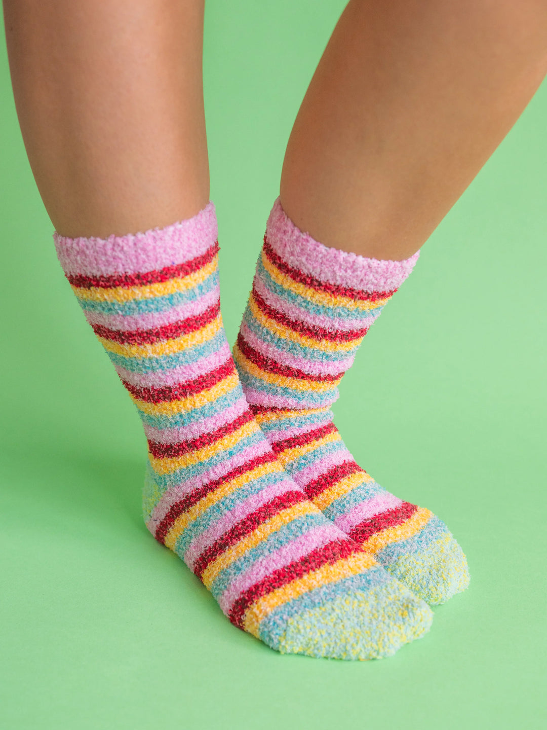 A pair of fuzzy, plush crew socks with a vibrant horizontal stripe pattern in a variety of rainbow-inspired colors.