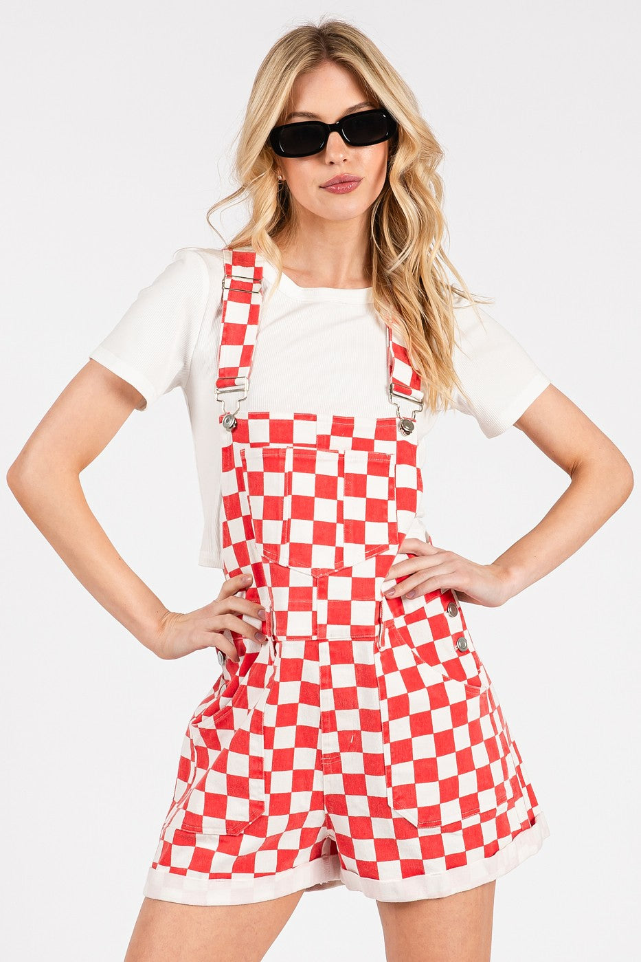 Red checkered knit romper overalls with adjustable straps, metal hardware, multiple pockets, and cuffed shorts, laid flat to highlight color and texture.