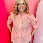 Blush pink floral button-down top with ruffled placket, puff sleeves, and tied-back detail.