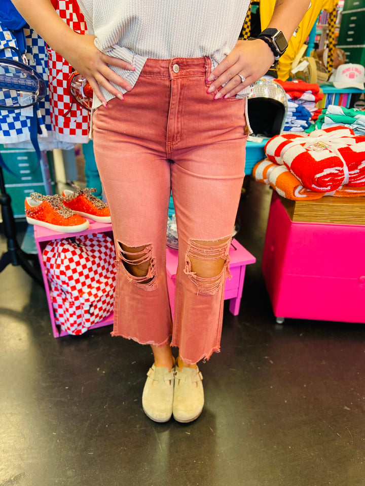 Close up of Cabernet colored jeans with cropped length and distressing at knees. Raw hem line.