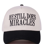 Black and white two-tone cap with “He Still Does Miracles” embroidered on the front.
