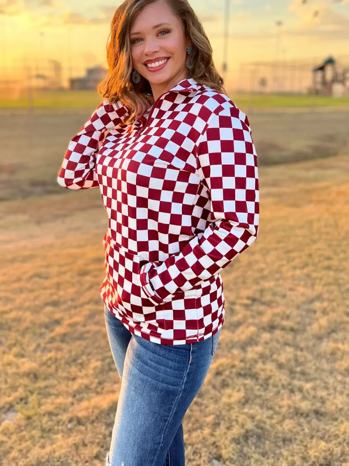 Maroon and white checkered pullover with a collared neckline, quarter-zip front, and kangaroo pocket, laid flat to showcase the bold pattern and design.