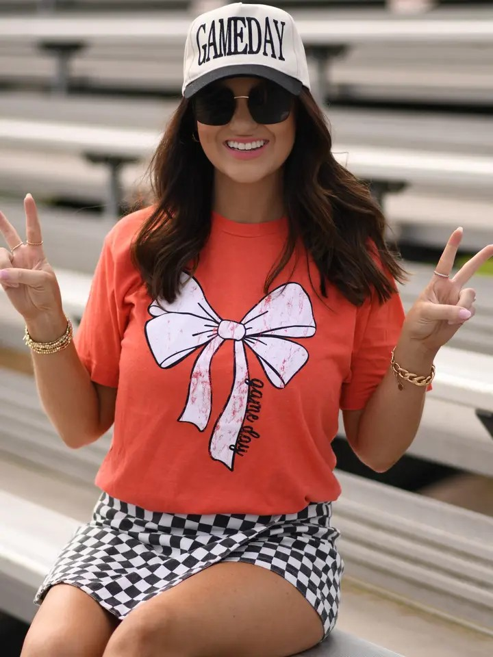 Orange Tultex tee with a white bow and bold black “game day” lettering at the bottom, laid flat for display.