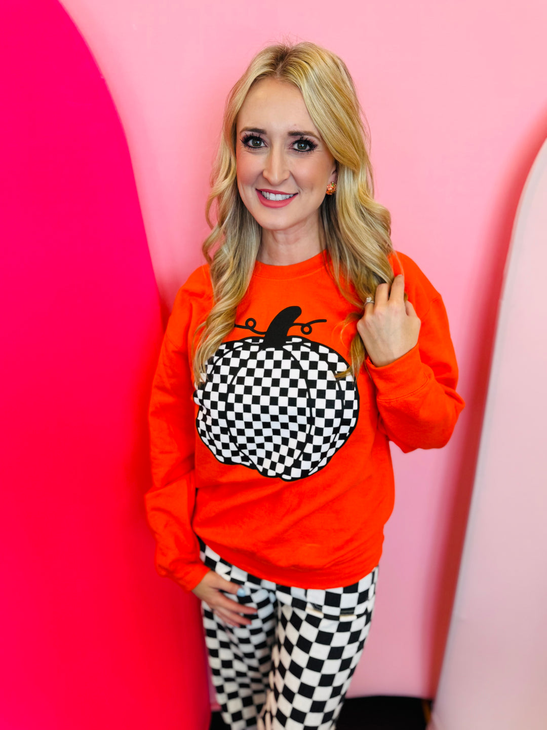 Orange crewneck sweatshirt with bold black and white checkered pumpkin graphic, perfect for fall