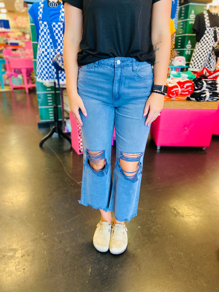 close up of Blackberry colored washed cropped jeans with distressed knees and raw hem