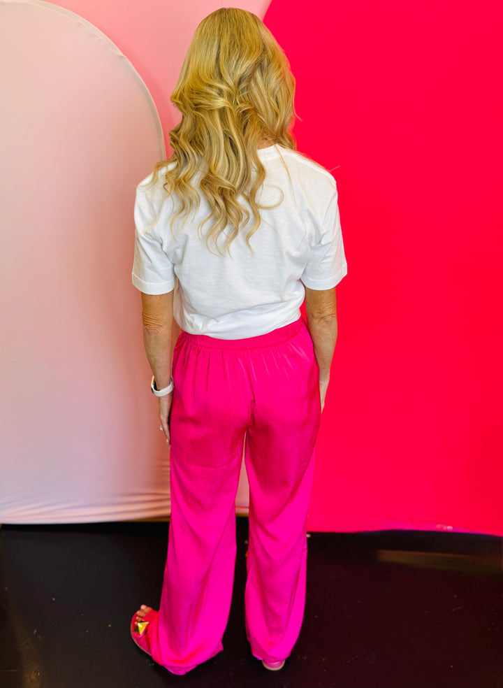 Back view of the hot pink pants highlighting the smooth satin finish, relaxed straight leg silhouette, and comfortable waistband fit.